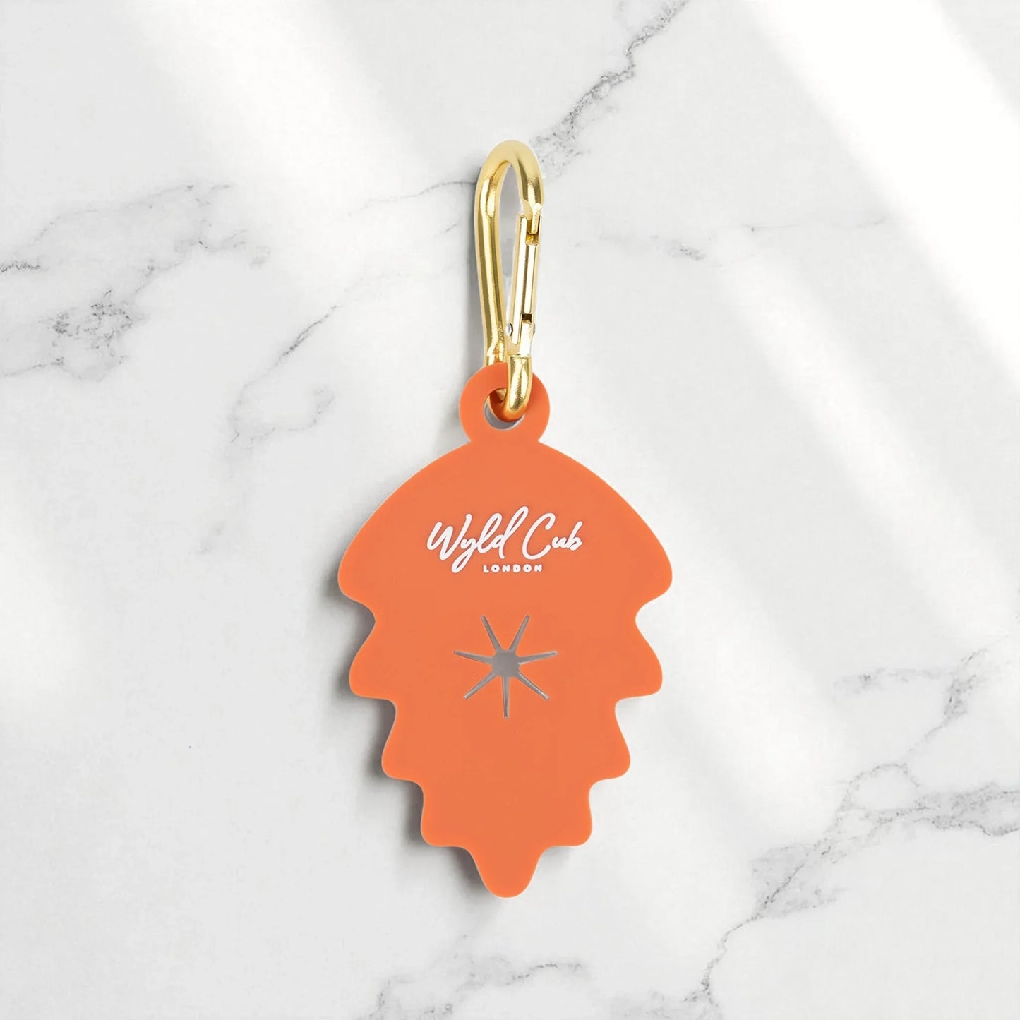 Orange Wyld Cub London keychain with gold carabiner on white marble surface